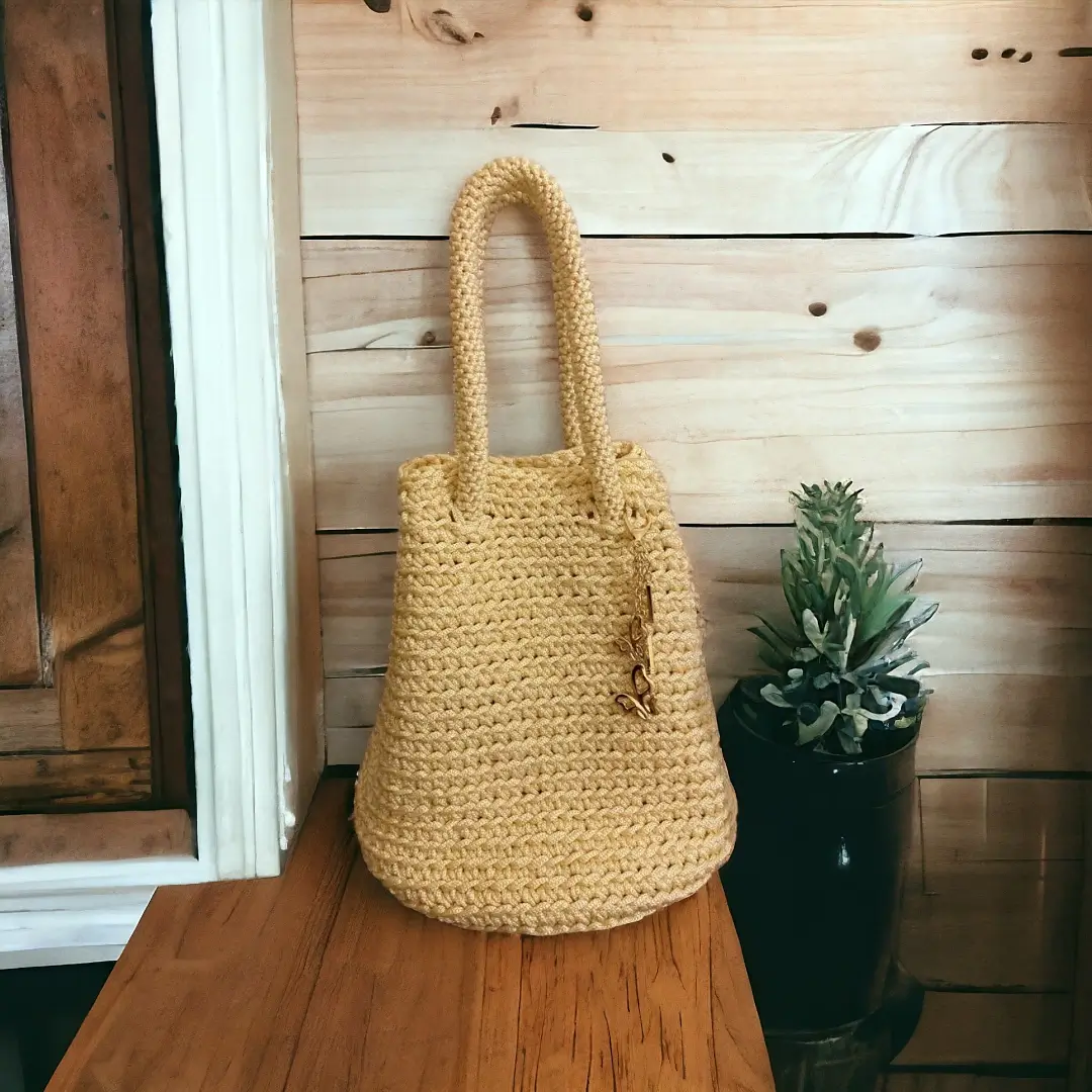mes-crations-crochellem-galerieweb (13) Sac tote n en crochet jaune moutarde posé sur une table en bois à côté d'une plante verte.