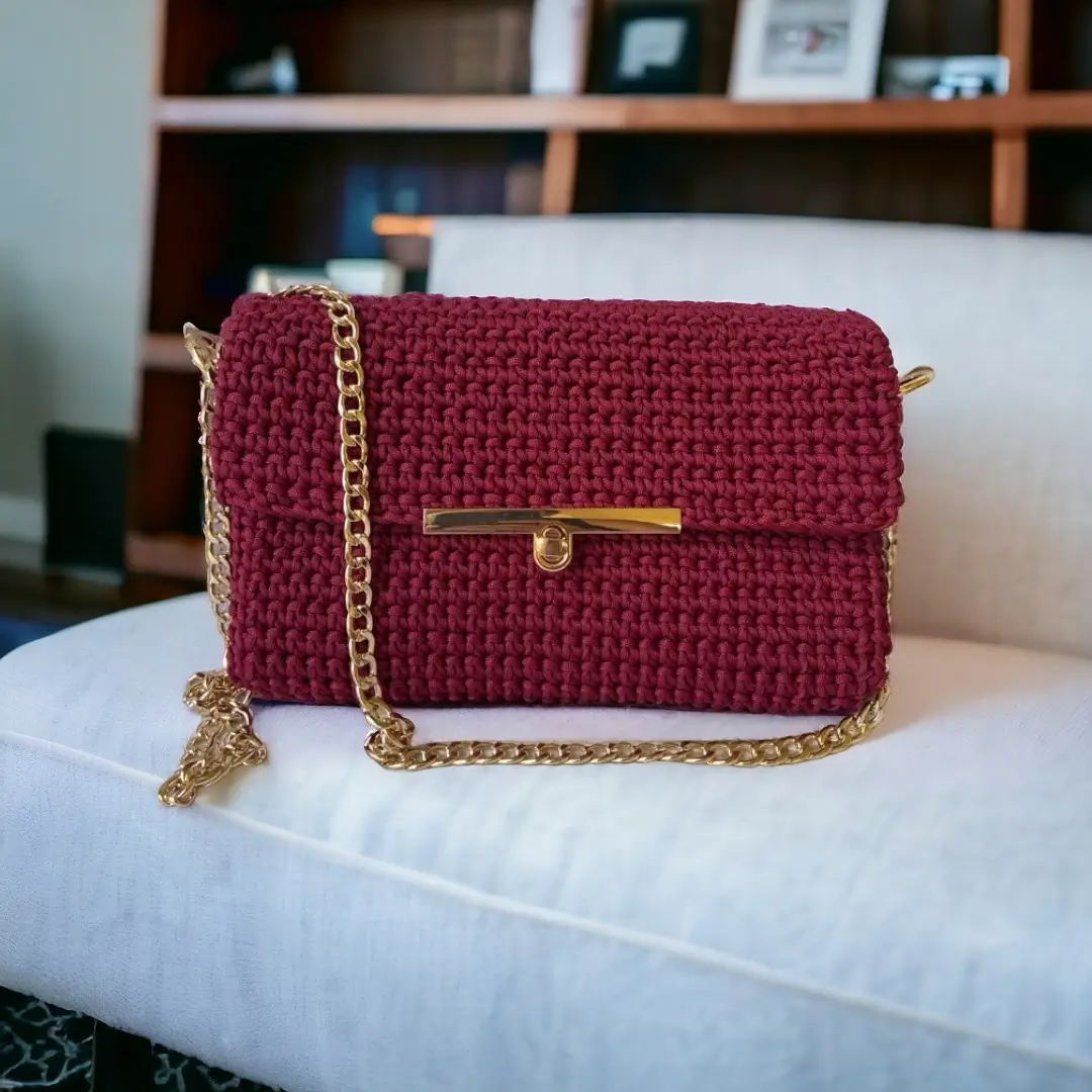 mes-crations-crochellem-galerieweb (14) Sac à bandoulière en crochet bordeaux avec chaîne dorée et fermoir métallique, posé sur un canapé clair.