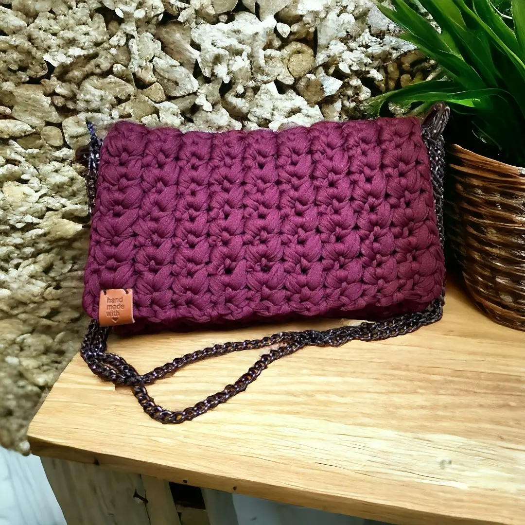 mes-crations-crochellem-galerieweb (18) Sac à bandoulière en crochet pourpre avec chaîne foncée et étiquette 'handmade', posé sur une étagère en bois.