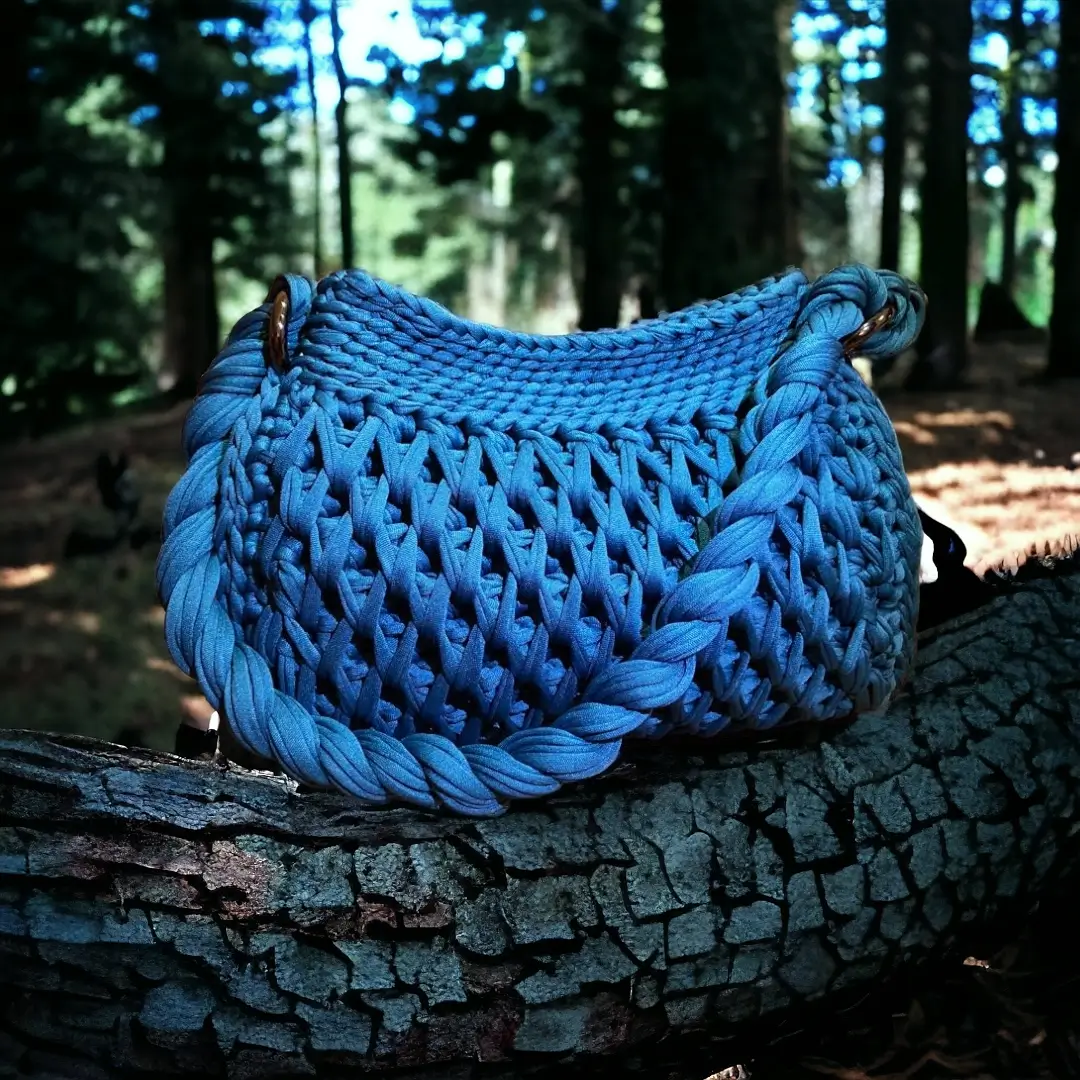 mes-crations-crochellem-galerieweb (20) Sac à main en maille bleue avec anse tressée, reposant sur un tronc d'arbre écorcé.