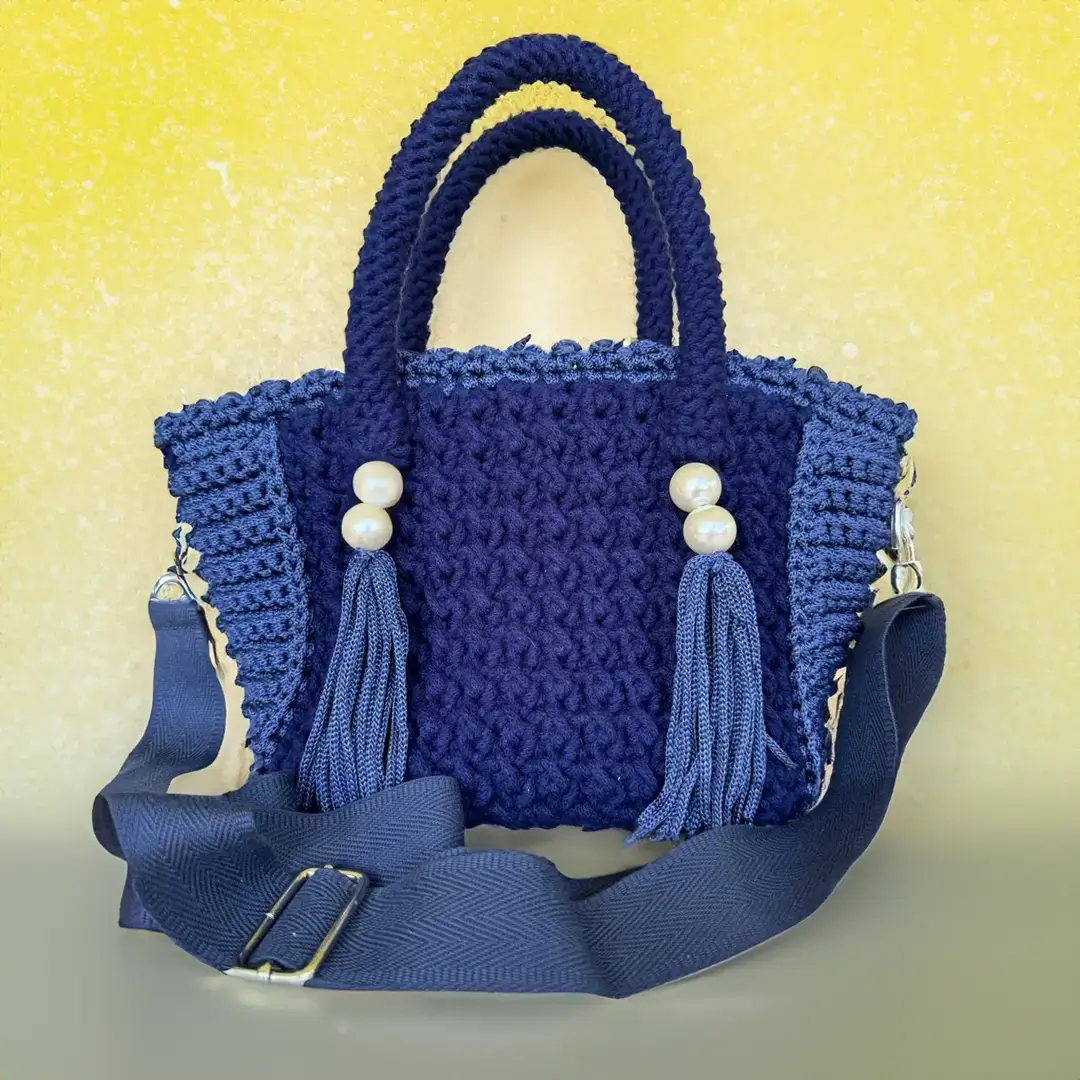 mes-crations-crochellem-galerieweb (22) Sac à main en crochet bleu marine avec perles et glands décoratifs, devant un paysage de plage tropicale.