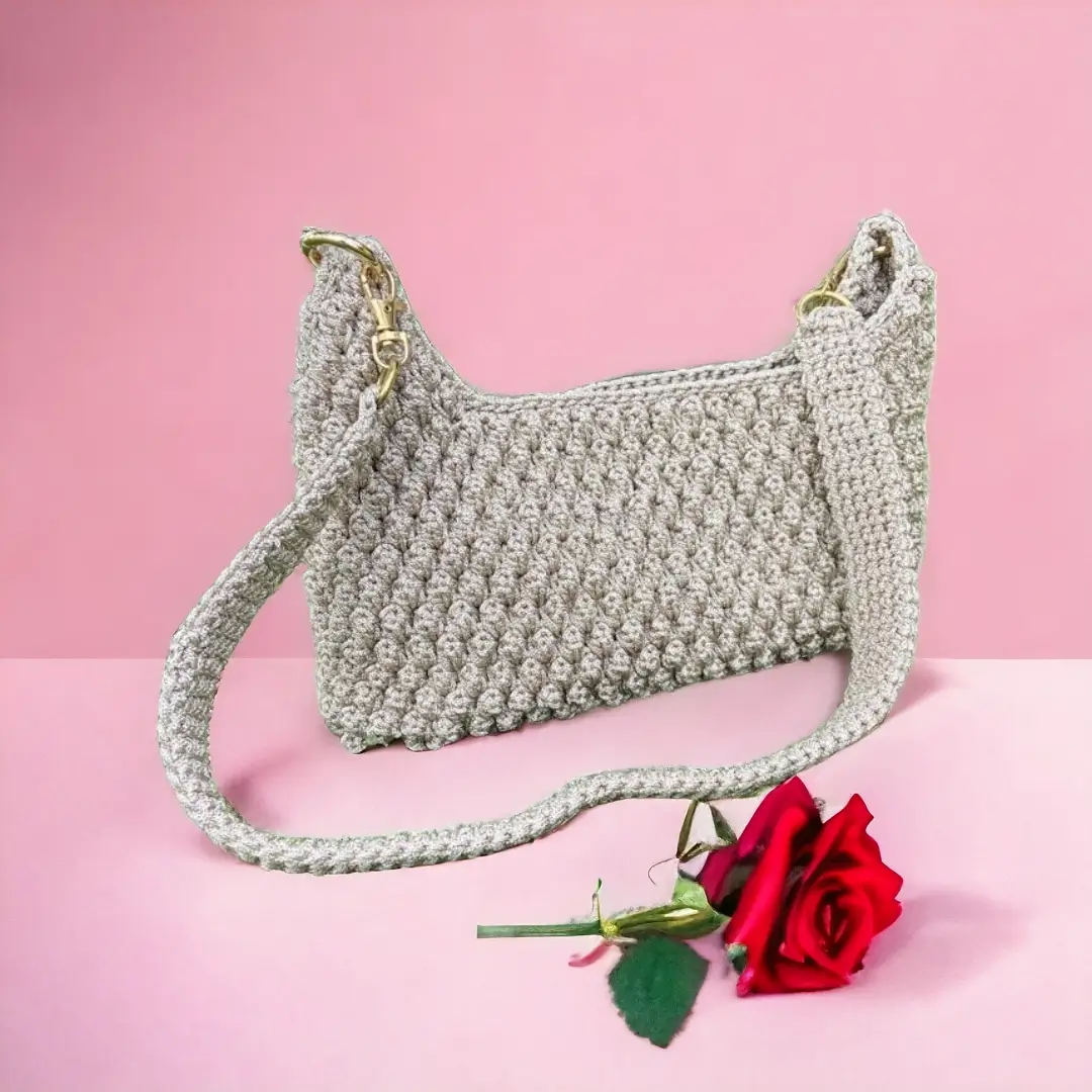 mes-crations-crochellem-galerieweb (25) Sac à bandoulière en crochet blanc avec fermetures dorées, présenté sur un fond rose avec une rose rouge.