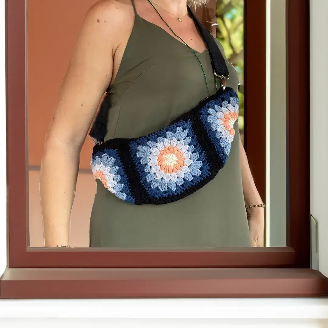 mes-crations-crochellem-galerieweb (45) Pochette en crochet à motif floral, mélangeant des teintes de bleu, d'orange et de blanc pour un style bohème et artisanal. Parfaite pour accessoiriser une tenue décontractée.