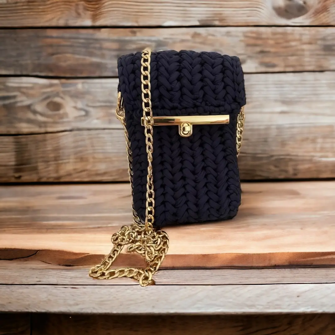 mes-crations-crochellem-galerieweb (5) Sac à bandoulière en crochet bleu marine avec une chaîne dorée et fermoir métallique, posé sur un banc en bois.