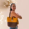 Sac cabas tricoté bicolore avec fermeture à bouton et pompon décoratif sur le côté porté par Emmanuelle