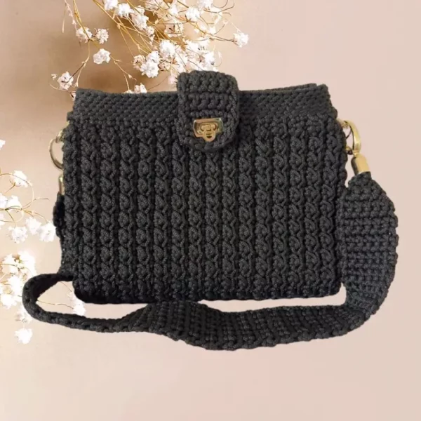 Sac à main noir en crochet avec texture côtelée, fermoir doré et bandoulière ajustable.