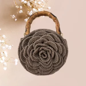 Sac à main crocheté en gris taupe avec motif floral en relief et anse en résine.