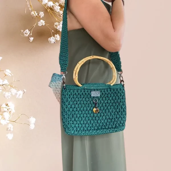 Sac à main en crochet vert émeraude avec anse en bambou et pendentif décoratif, porté à lpaule par mannequin