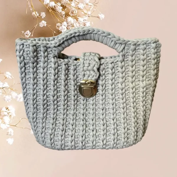 Un sac panier en crochet de couleur gris clair, orné d'une fermeture métallique vintage argenté, combine esthétique traditionnelle et praticité moderne, vue de face