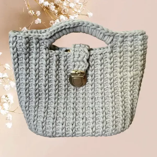Un sac panier en crochet de couleur gris clair, orné d'une fermeture métallique vintage argenté, combine esthétique traditionnelle et praticité moderne, vue de face