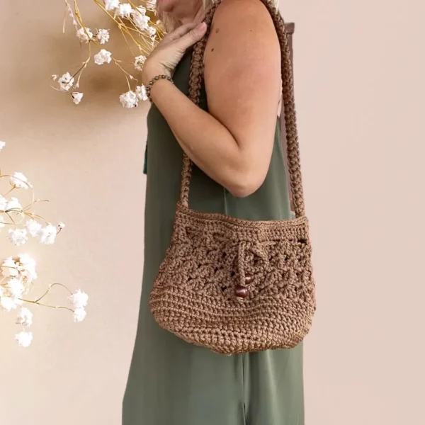 Sac seau en crochet marron avec cordon et perles de bois sur fond rose pâle, porté par mannequin