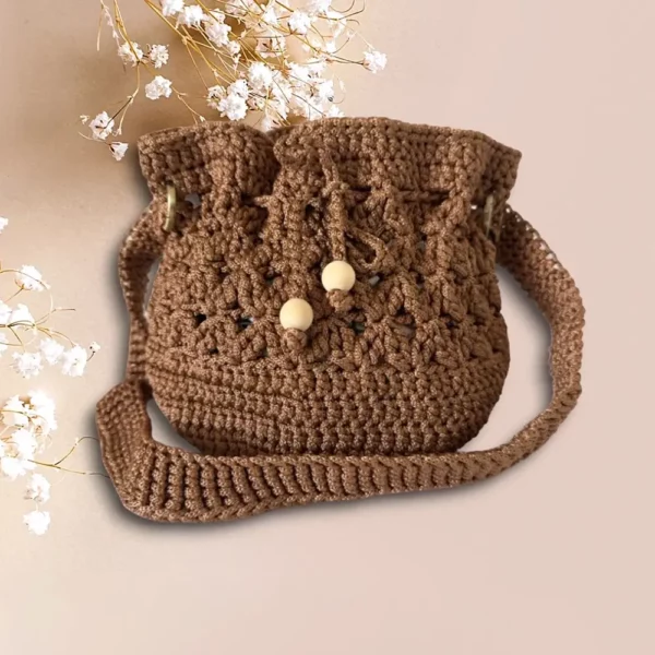 Sac seau en crochet marron avec cordon et perles de bois sur fond rose pâle