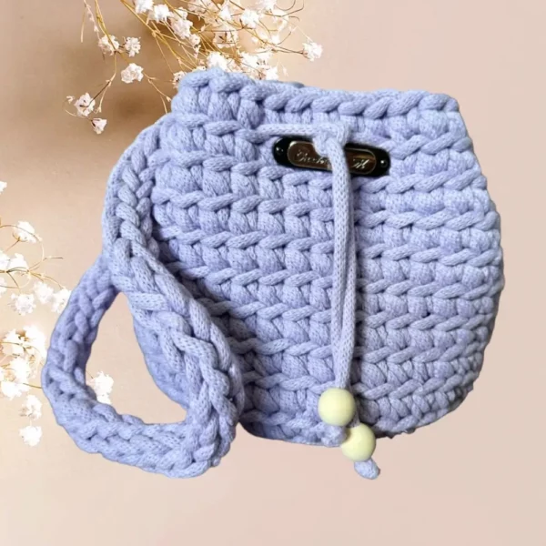 Un tote bag en crochet de couleur lilas, avec une fermeture à cordon agrémentée de perles pastel, idéal pour une touche de douceur et de style à votre garde-robe, vue de face