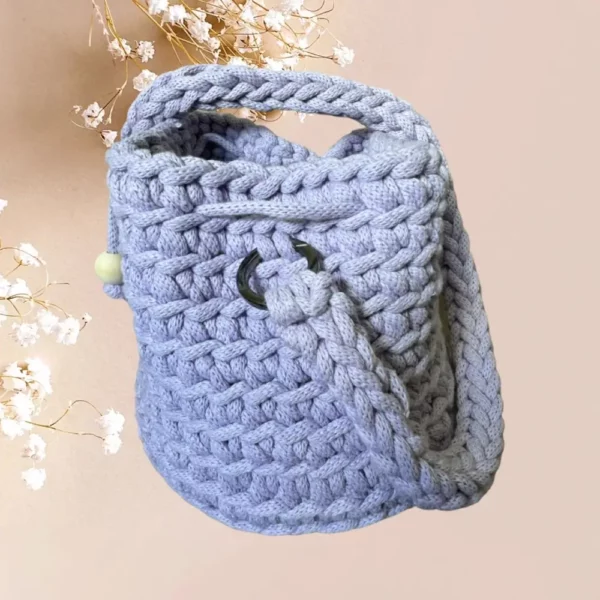 Un tote bag en crochet de couleur lilas, avec une fermeture à cordon agrémentée de perles pastel, idéal pour une touche de douceur et de style à votre garde-robe, vue de profil